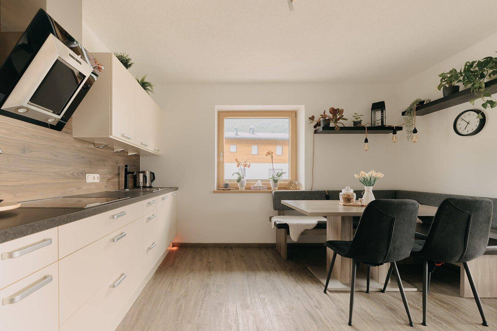 Moderne Küche mit weißen Schränken, Holzakzenten und Essbereich am Fenster.