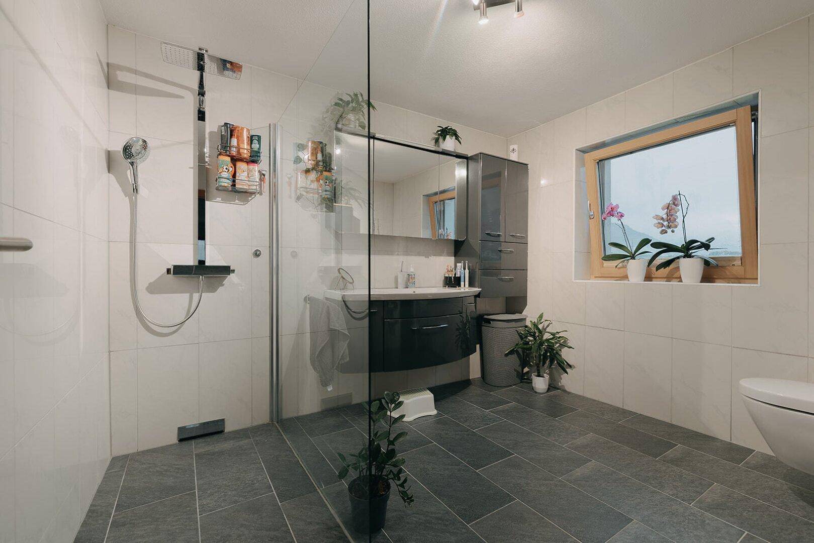Helles Badezimmer mit begehbarer Dusche, Waschtisch und Fenster für Tageslicht.