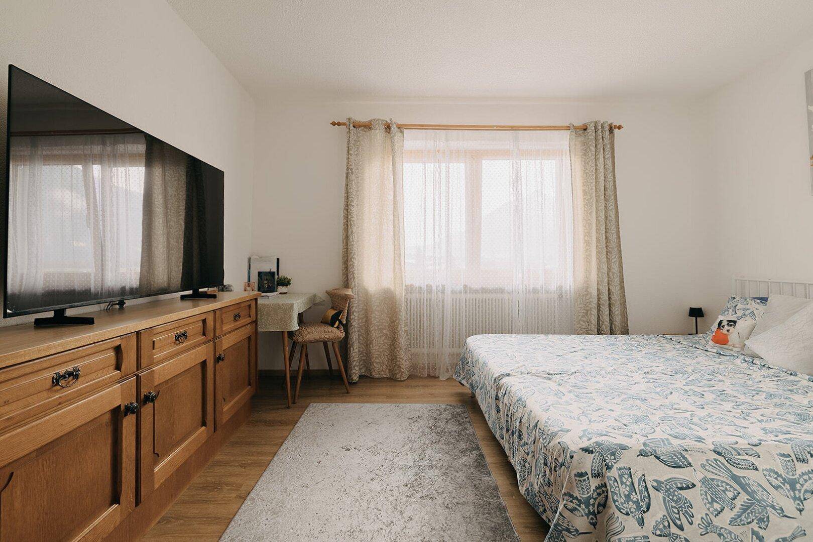 Schlafzimmer mit großem Fernseher, Holzmöbeln und hellem Laminatboden.