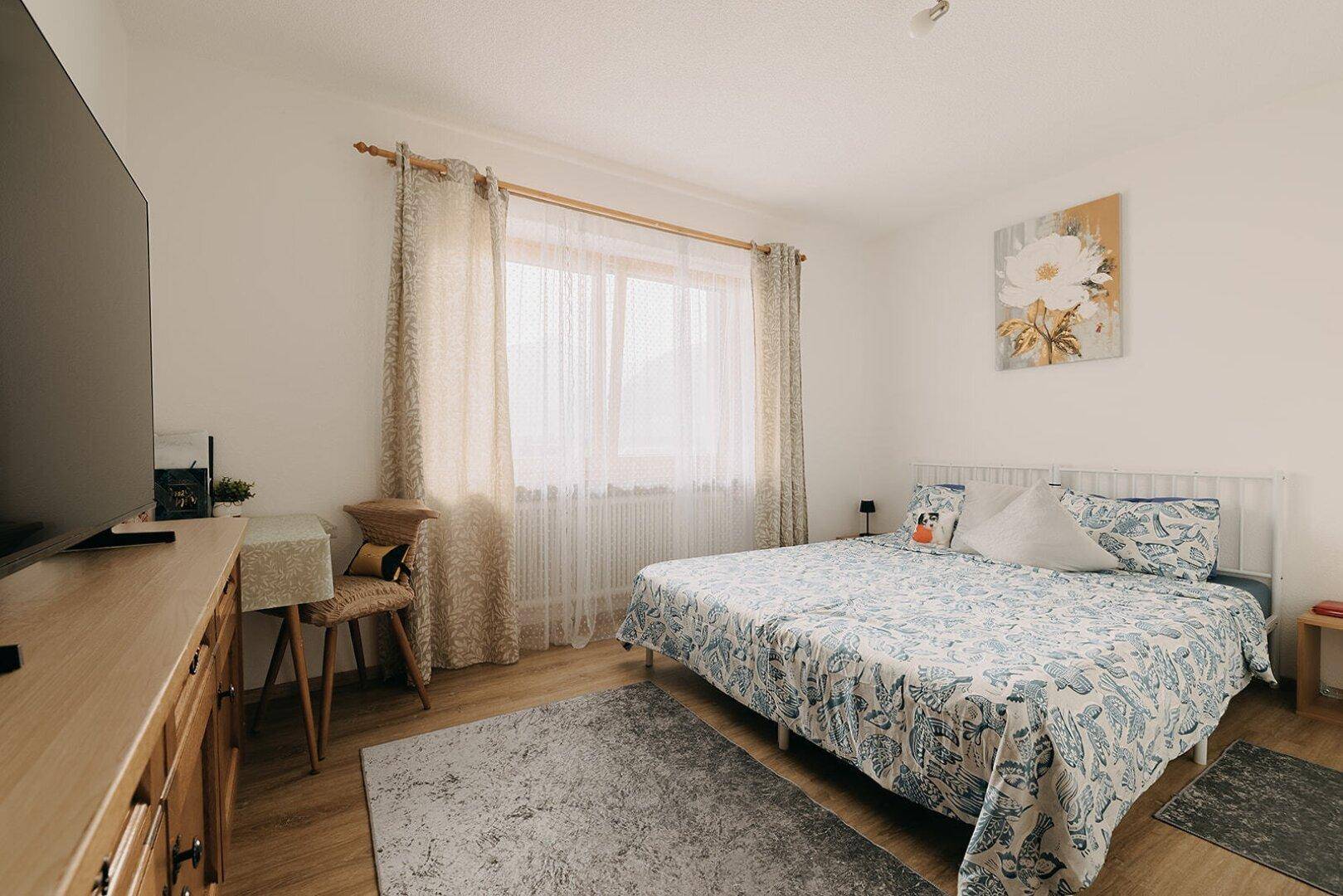 Gemütliches Schlafzimmer mit Doppelbett, Holzboden und großem Fenster für viel Tageslicht.