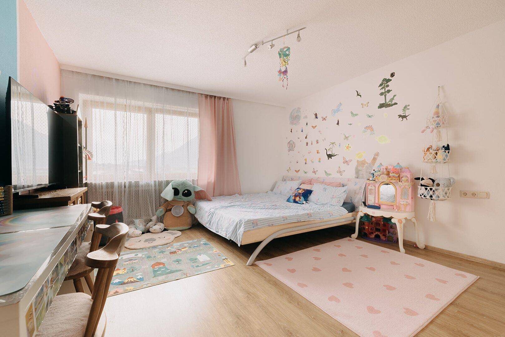 Helles Schlafzimmer mit Holzboden, Schreibtisch und verspielter Wanddekoration für Kinder.