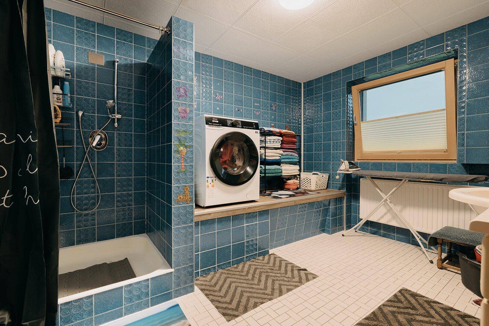 Funktionaler Waschraum mit Dusche, Waschmaschine und blauen Fliesen.