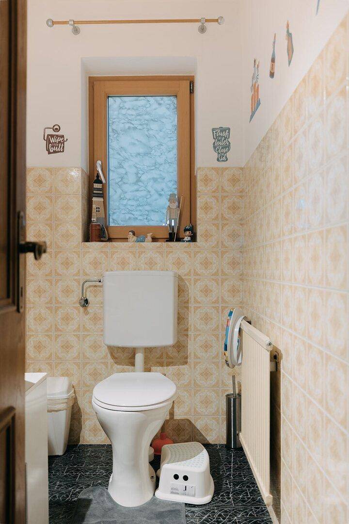 Kleines WC mit Fenster, beigen Fliesen und traditioneller Einrichtung.