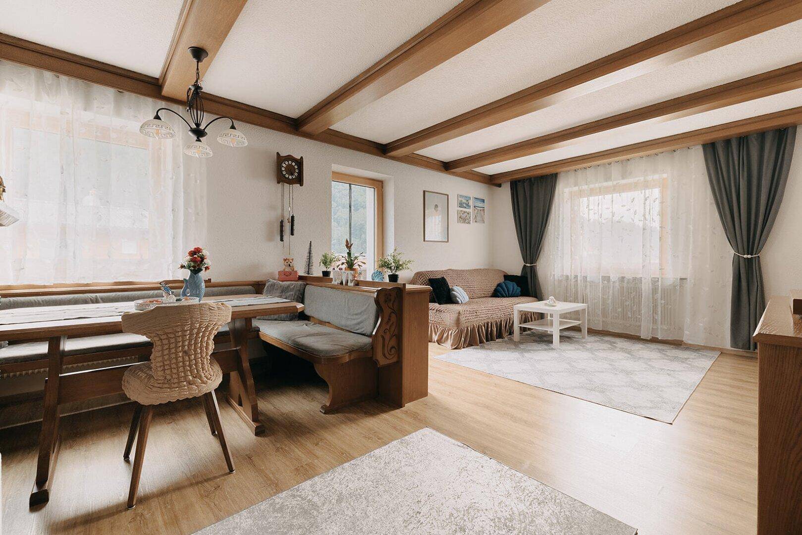 Gemütlicher Wohn-Essbereich mit Holzbalken, traditionellen Möbeln und viel Tageslicht.