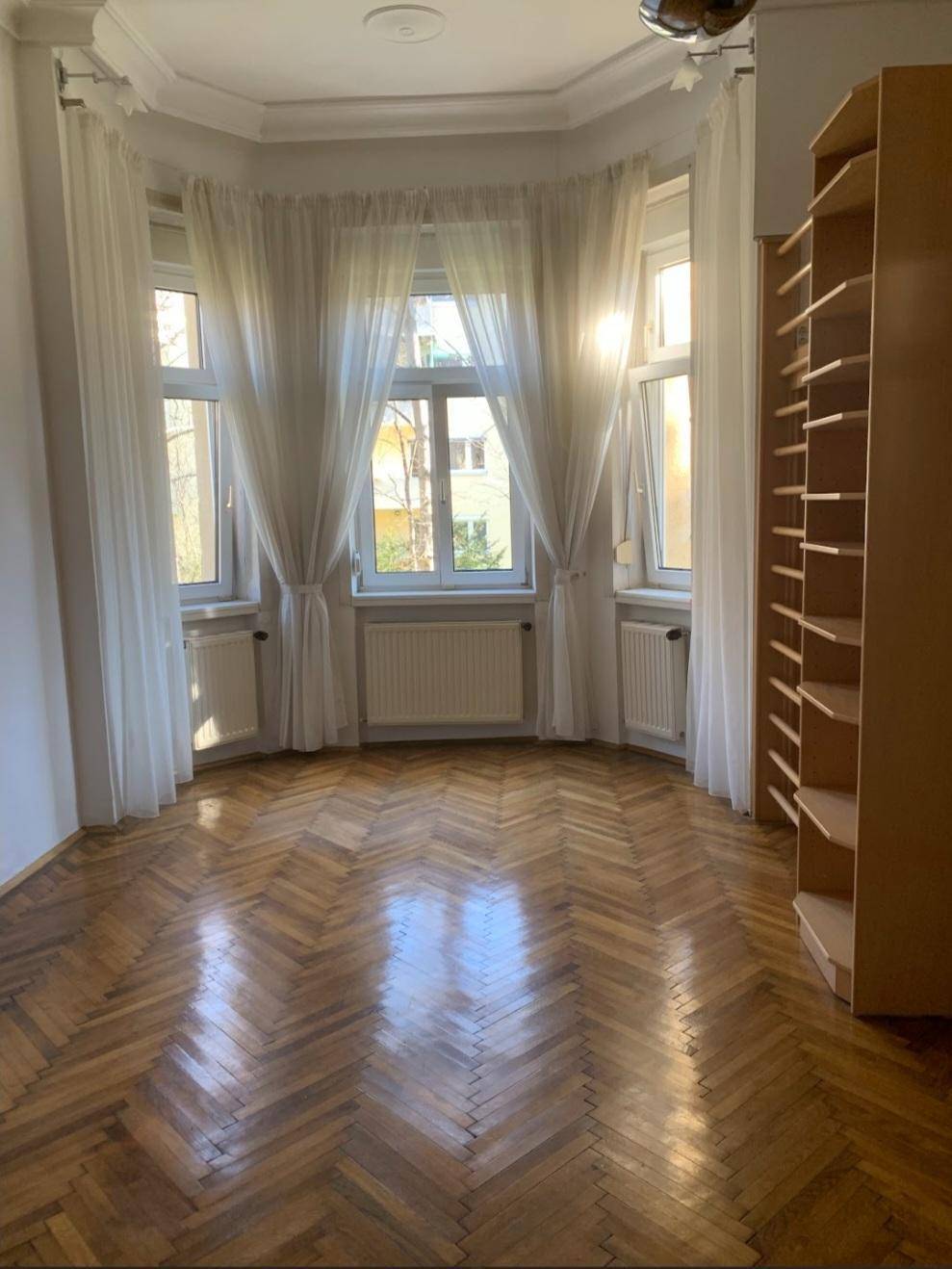 Lichtdurchflutetes Zimmer mit klassischem Fischgrätparkett und großen Fenstern mit Blick ins Grüne.