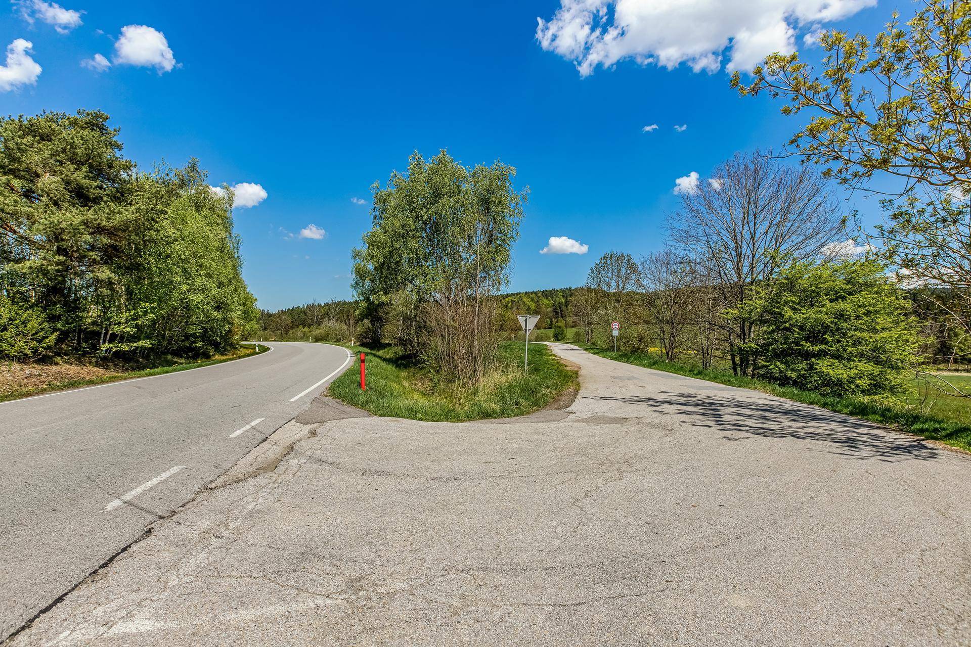 Eine ländliche Straßenkreuzung umgeben von Bäumen und grüner Vegetation unter einem strahlend blauen Himmel.