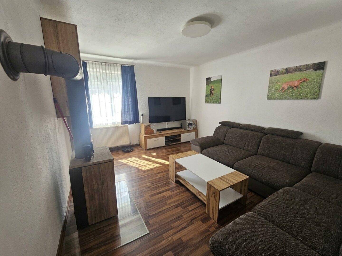 Gemütliches Wohnzimmer mit großem Sofa, Holzboden und einem modernen Holzofen für zusätzliche Wärme.