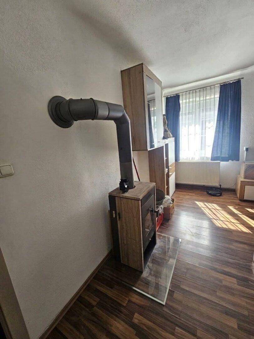 Detailansicht des modernen Holzofens mit sichtbarem Ofenrohr und Glasschutzplatte auf dem Boden.