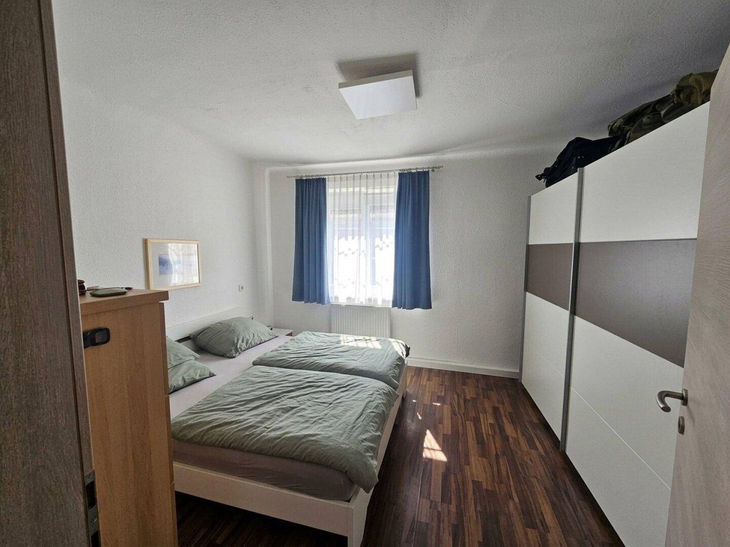 Helles Schlafzimmer mit Doppelbett, großem Kleiderschrank und Laminatboden.