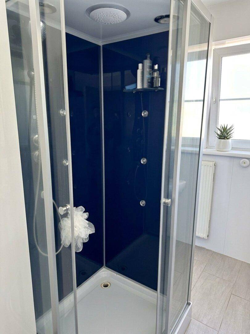 Moderne Duschkabine mit mehreren Massagedüsen und einer Regendusche, neben einem Fenster.