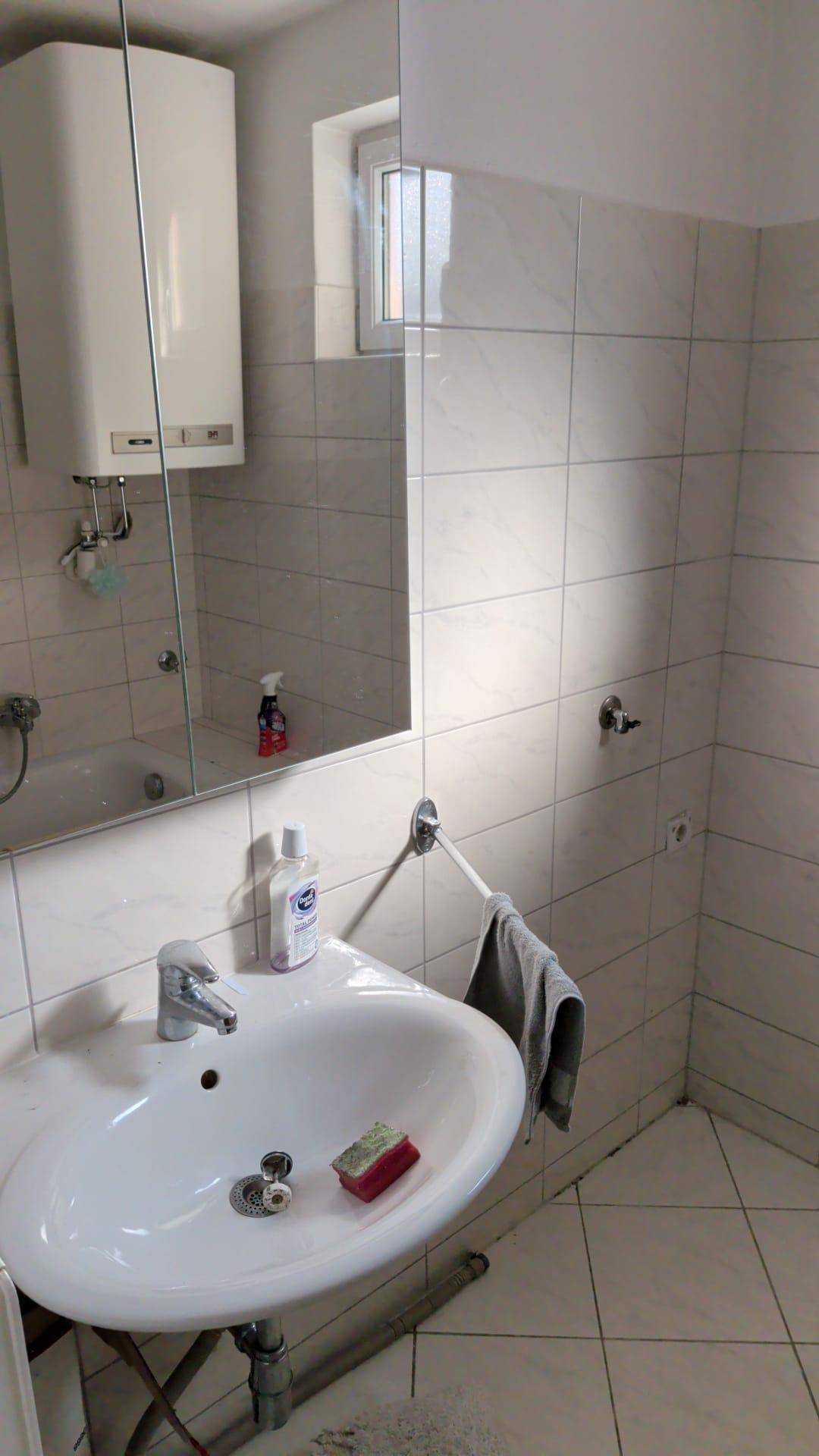Badezimmer mit weißen Fliesen, Einzelwaschbecken und einem Spiegelschrank.