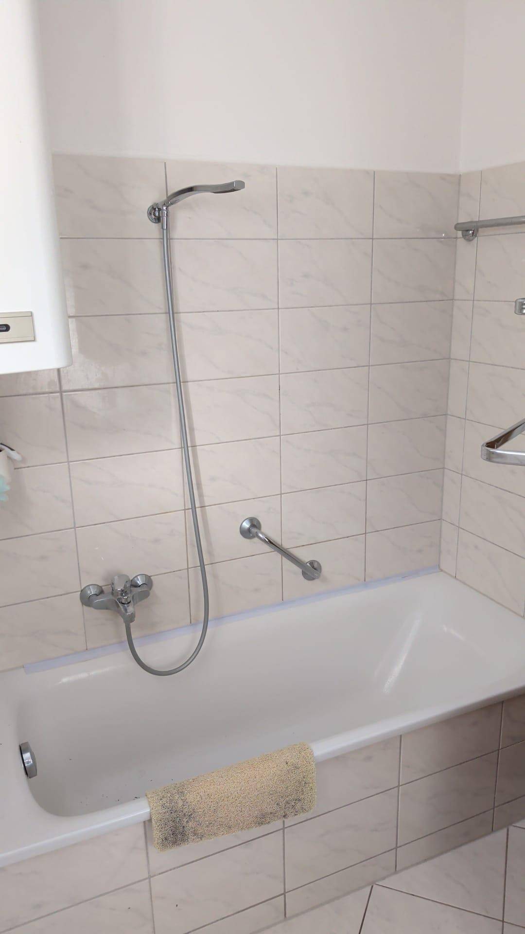 Badezimmer mit Badewanne und Duscharmatur, umgeben von hellen Fliesen.