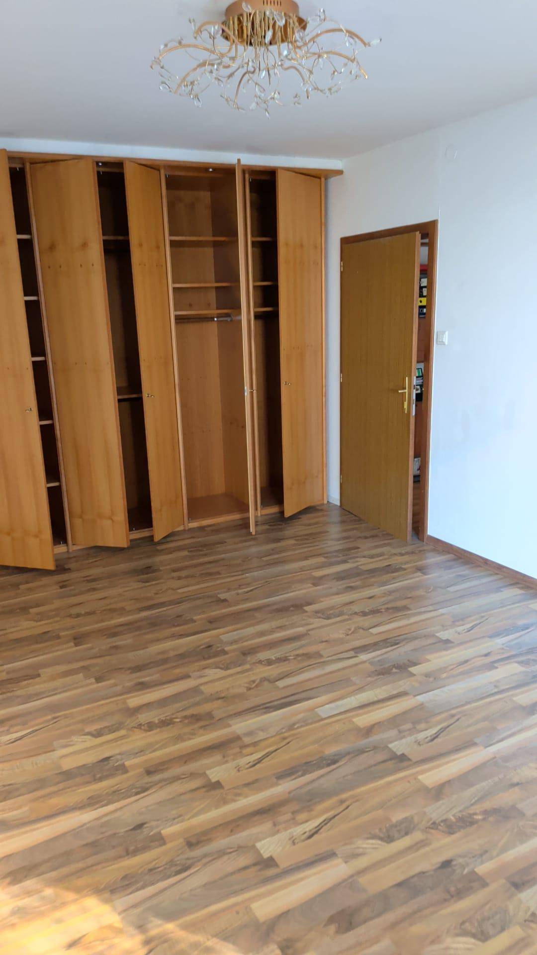 Schlafzimmer mit geöffneten Holzschränken, Parkettboden und einem dekorativen Deckenleuchter.