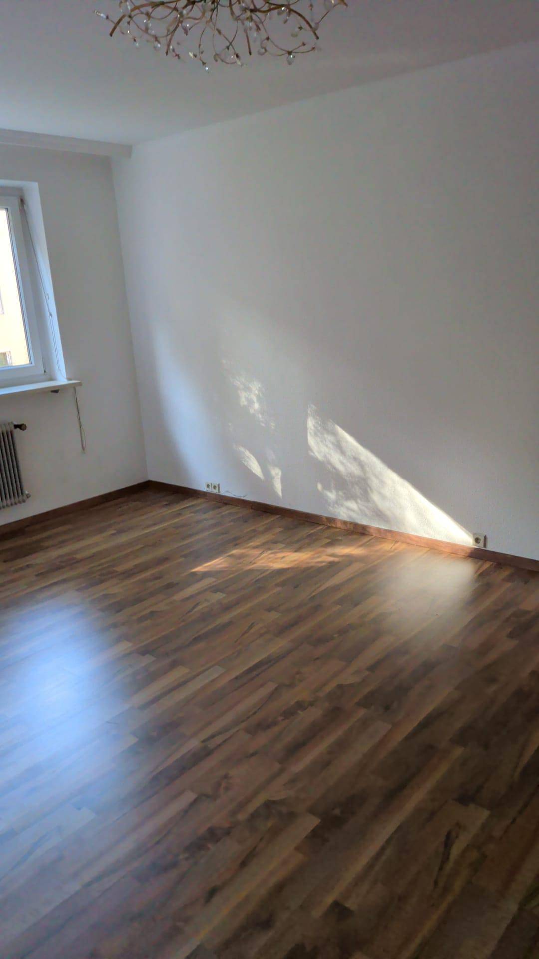 Heller Wohnraum mit Parkettboden und einem Fenster, das Sonnenlicht in den Raum bringt.