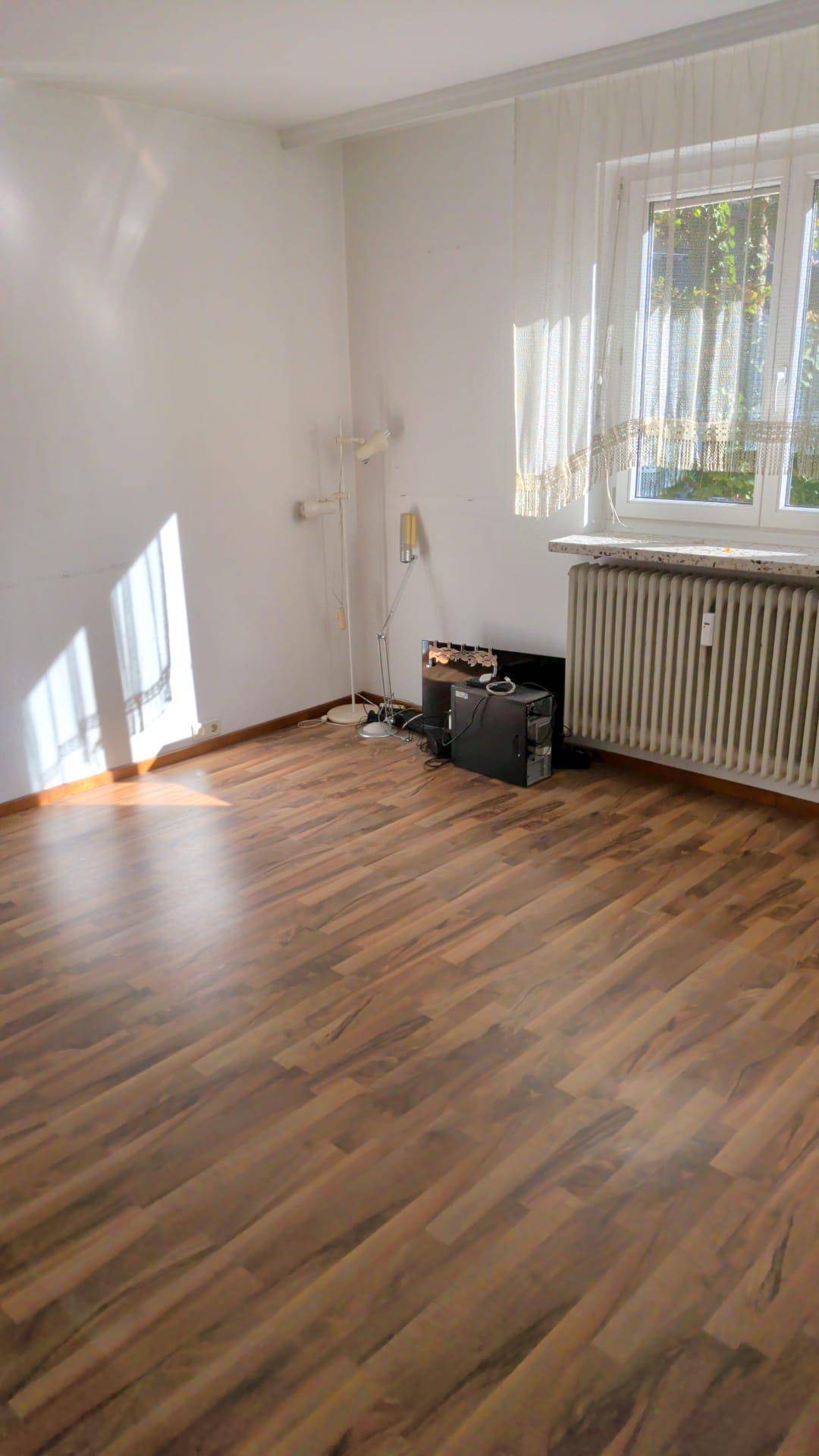 Heller Wohnraum mit Parkettboden und einem großen Fenster, das viel Licht hereinlässt.