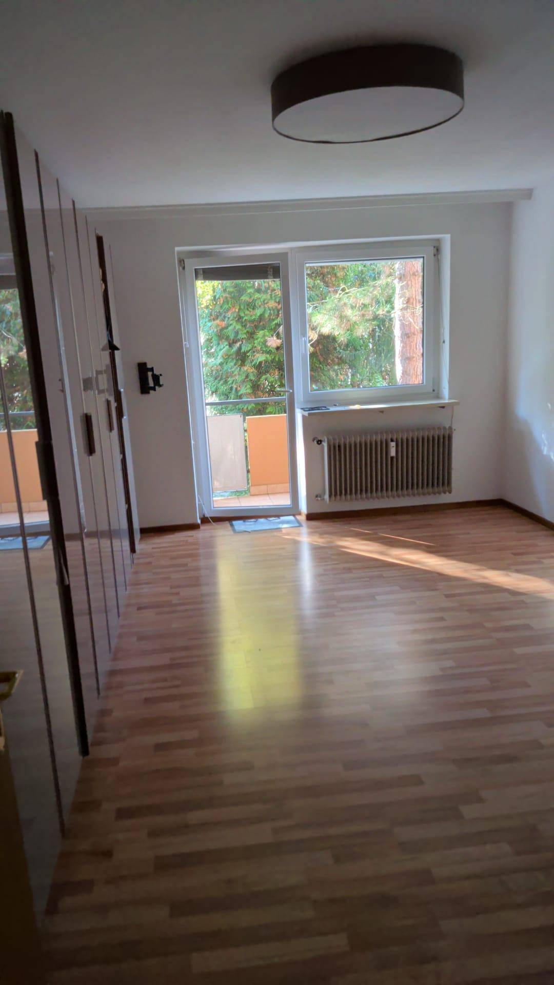 Heller Raum mit Parkettboden, großem Fenster und Zugang zu einem Balkon.