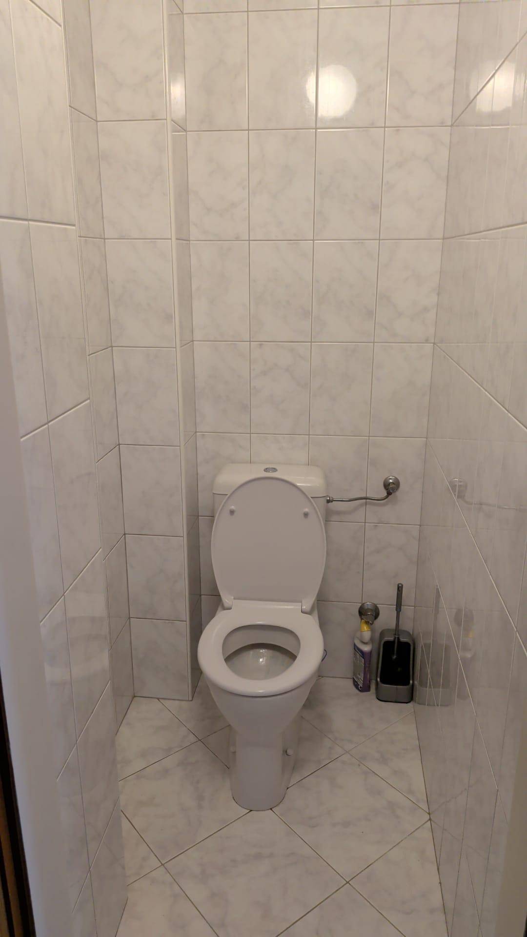 Separates WC mit weißen Fliesen und Standard-Toilette.