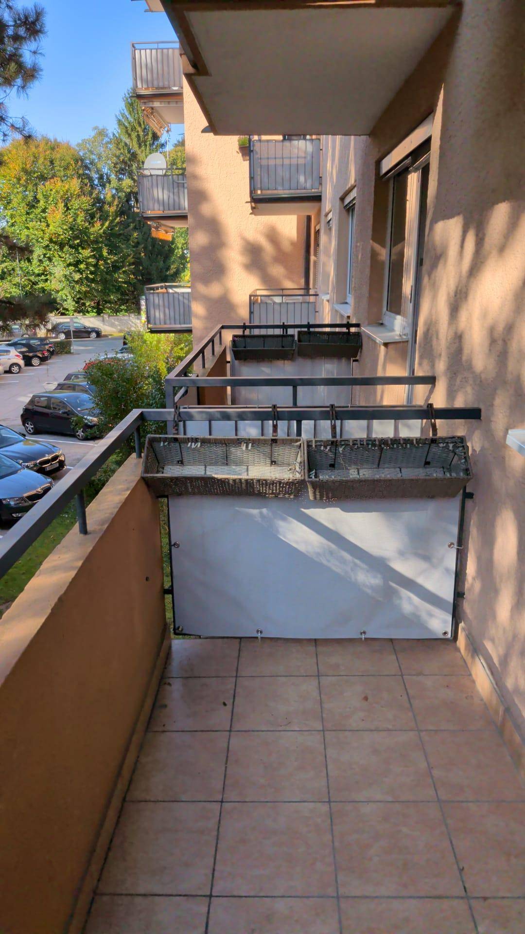 Balkon mit Fliesenboden und Blick auf die umliegenden Gebäude und Bäume.