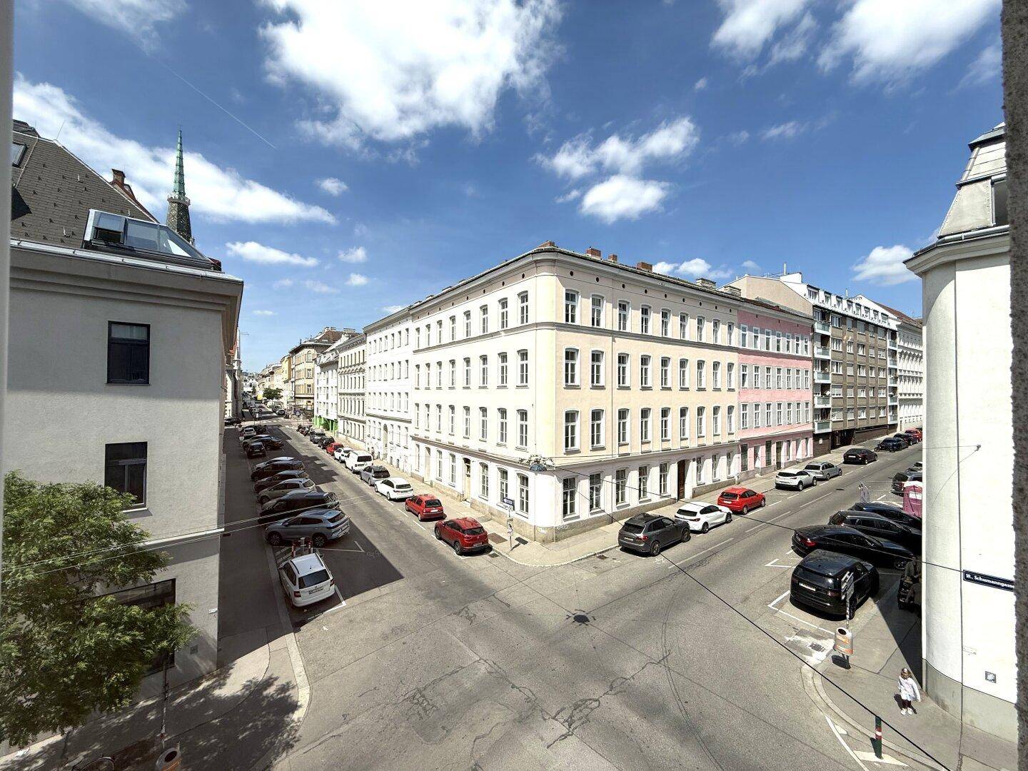 Blick von oben auf eine belebte Straßenkreuzung mit parkenden Autos und historischen Gebäuden.