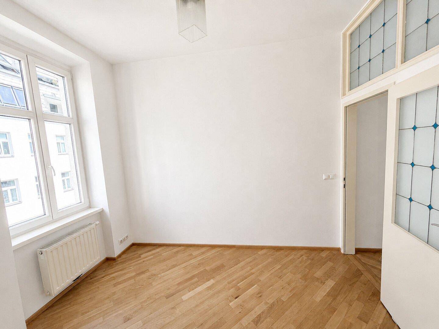 Helles Schlafzimmer mit Fischgrätparkett und einem Fenster mit Blick auf die Stadt.