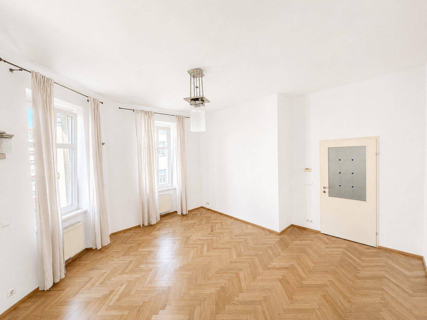 Lichtdurchflutetes Zimmer mit klassischem Fischgrätparkett und hohen Fenstern, typisch für Altbauten.