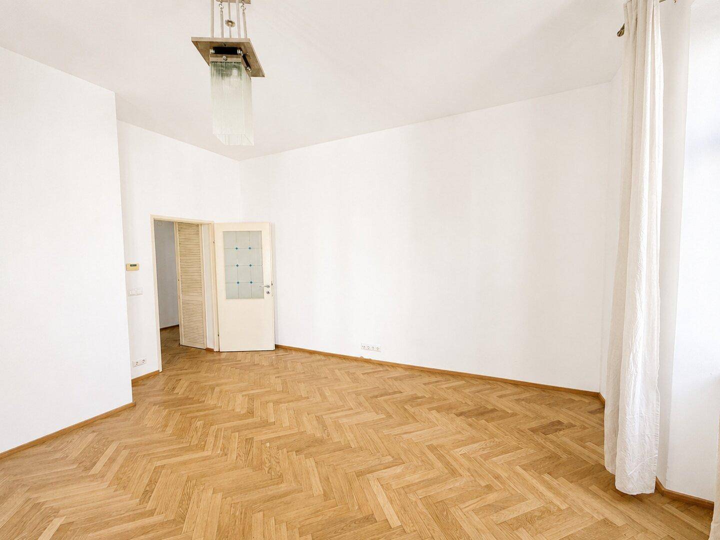 Geräumiges Zimmer mit Fischgrätparkett und einer Falttür, die zu einem angrenzenden Bereich führt.