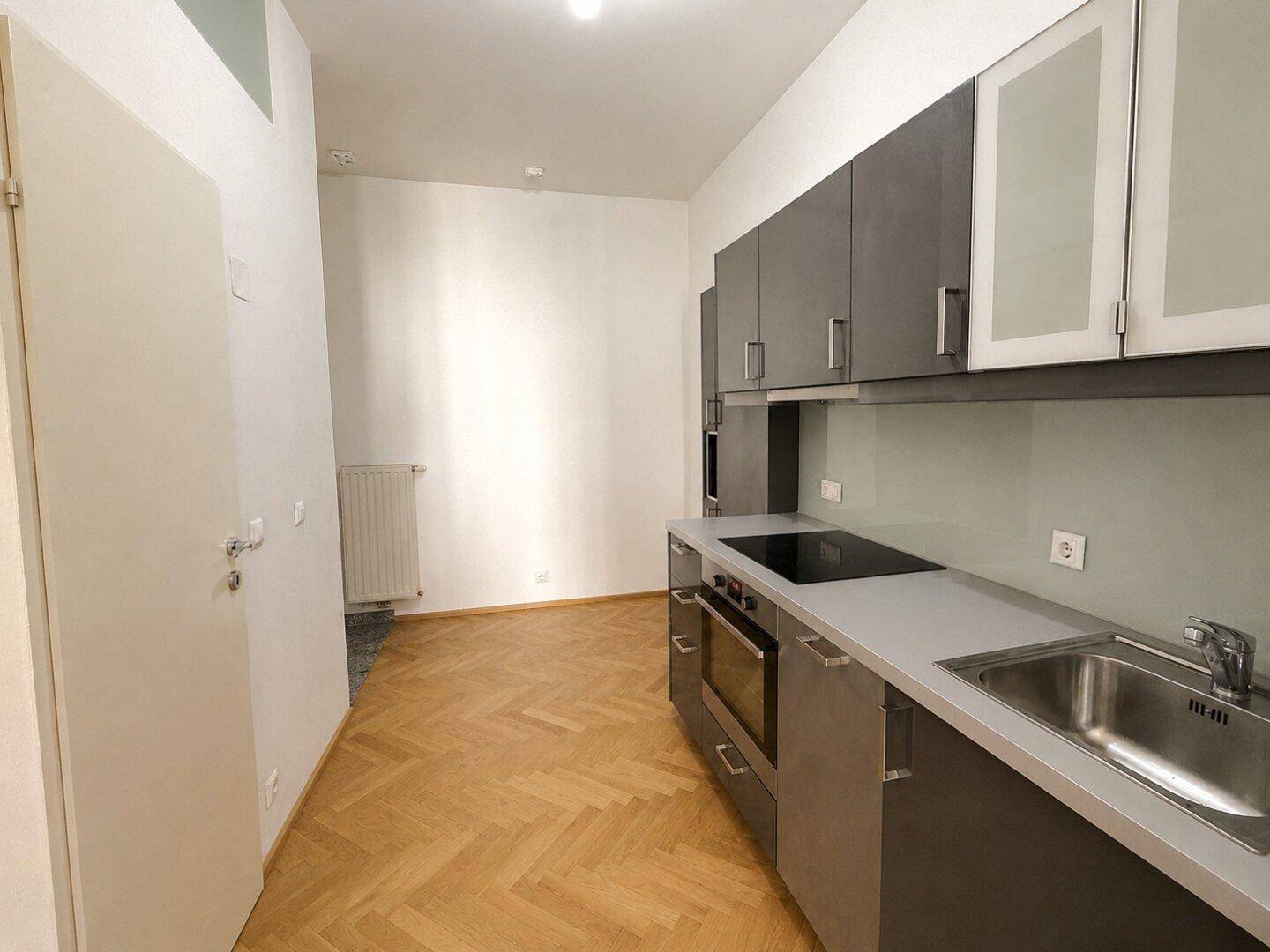 Moderne Einbauküche mit grauen Hochglanzfronten, Induktionskochfeld und integriertem Backofen.