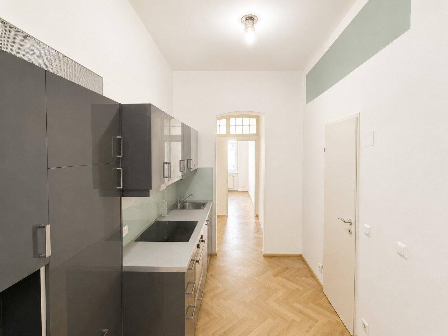 Moderne Küche mit grauen Schränken und Blick in den angrenzenden Flur mit Parkettboden.