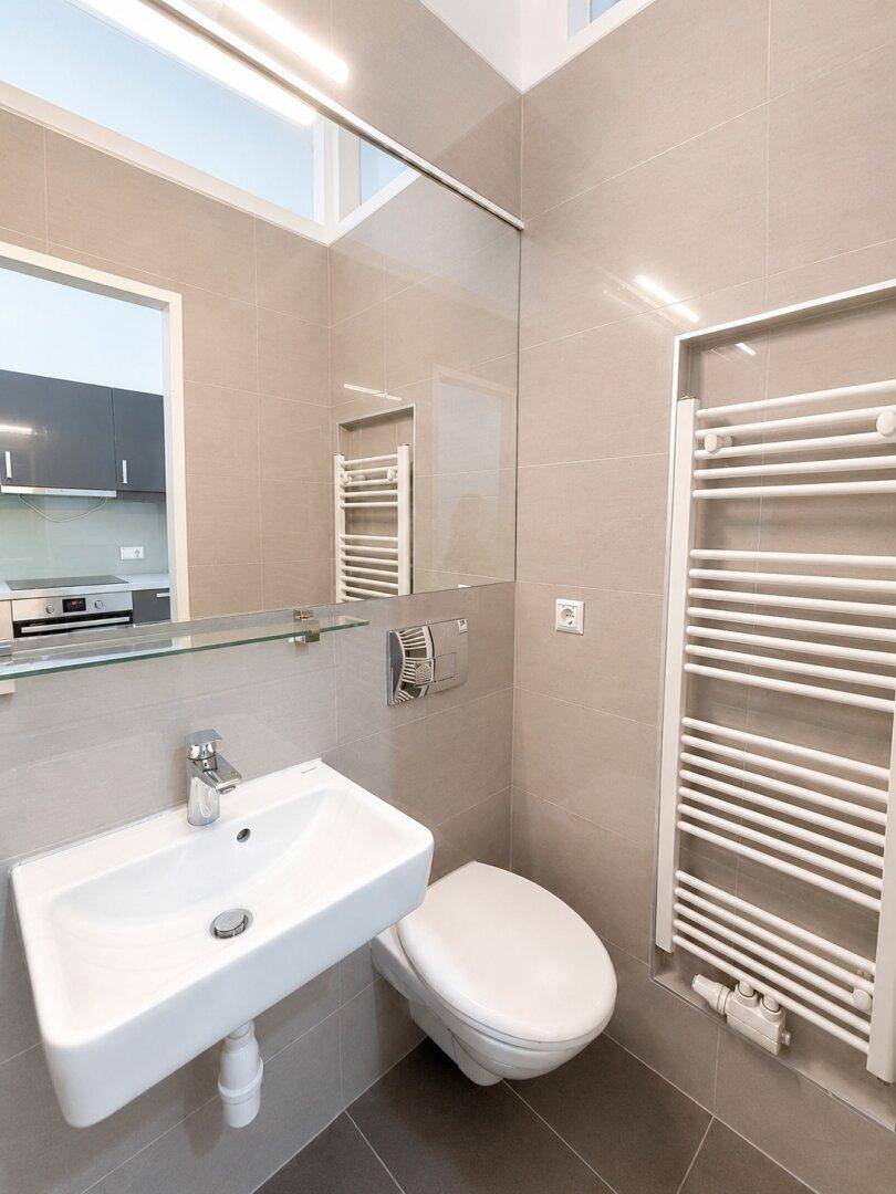Modernes Badezimmer mit Wandwaschbecken, wandhängendem WC und großem Spiegel über dem Waschtisch.