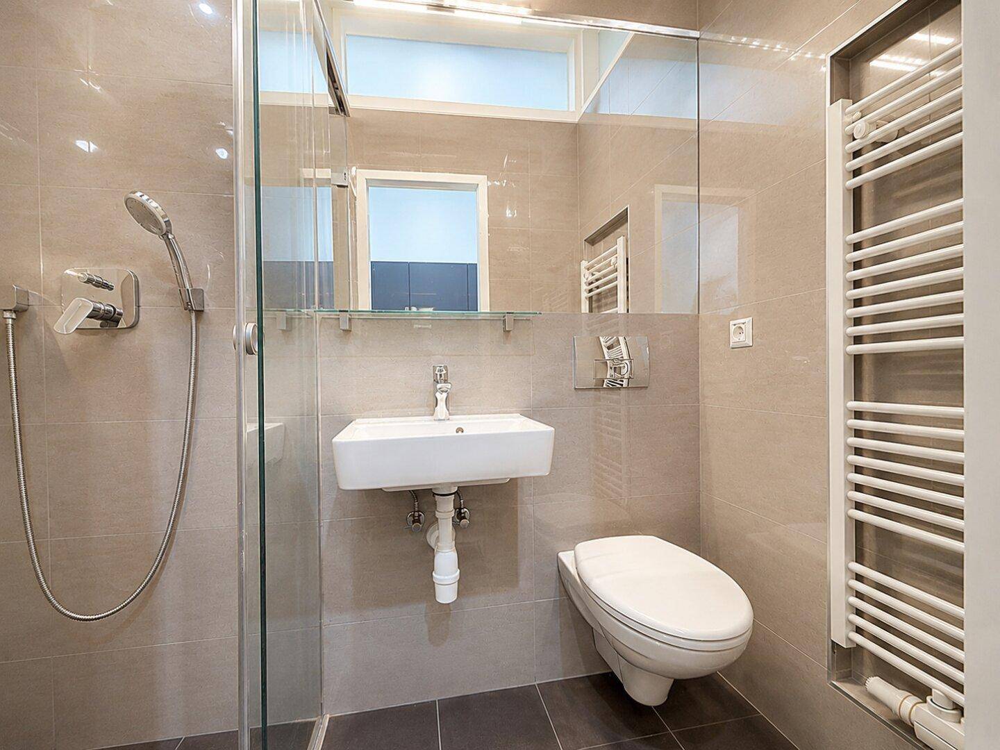Helles Badezimmer mit moderner Dusche, wandhängendem WC und beheiztem Handtuchhalter.