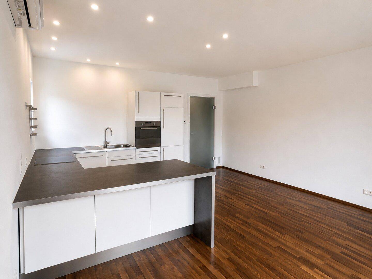 Moderne Einbauküche mit weißen Hochglanzfronten, dunkler Arbeitsplatte und integriertem Backofen.