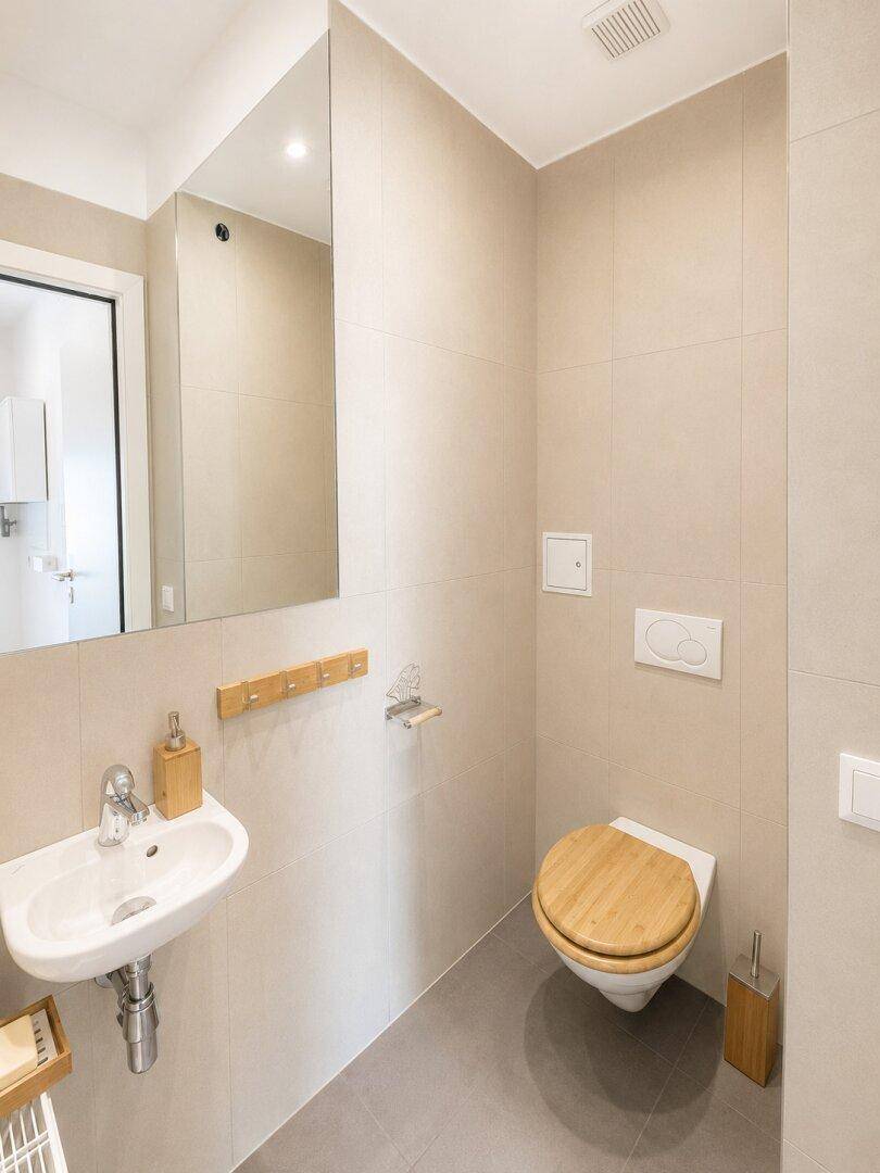 Gäste-WC mit kleinem Waschbecken, wandhängender Toilette und beigen Fliesen.