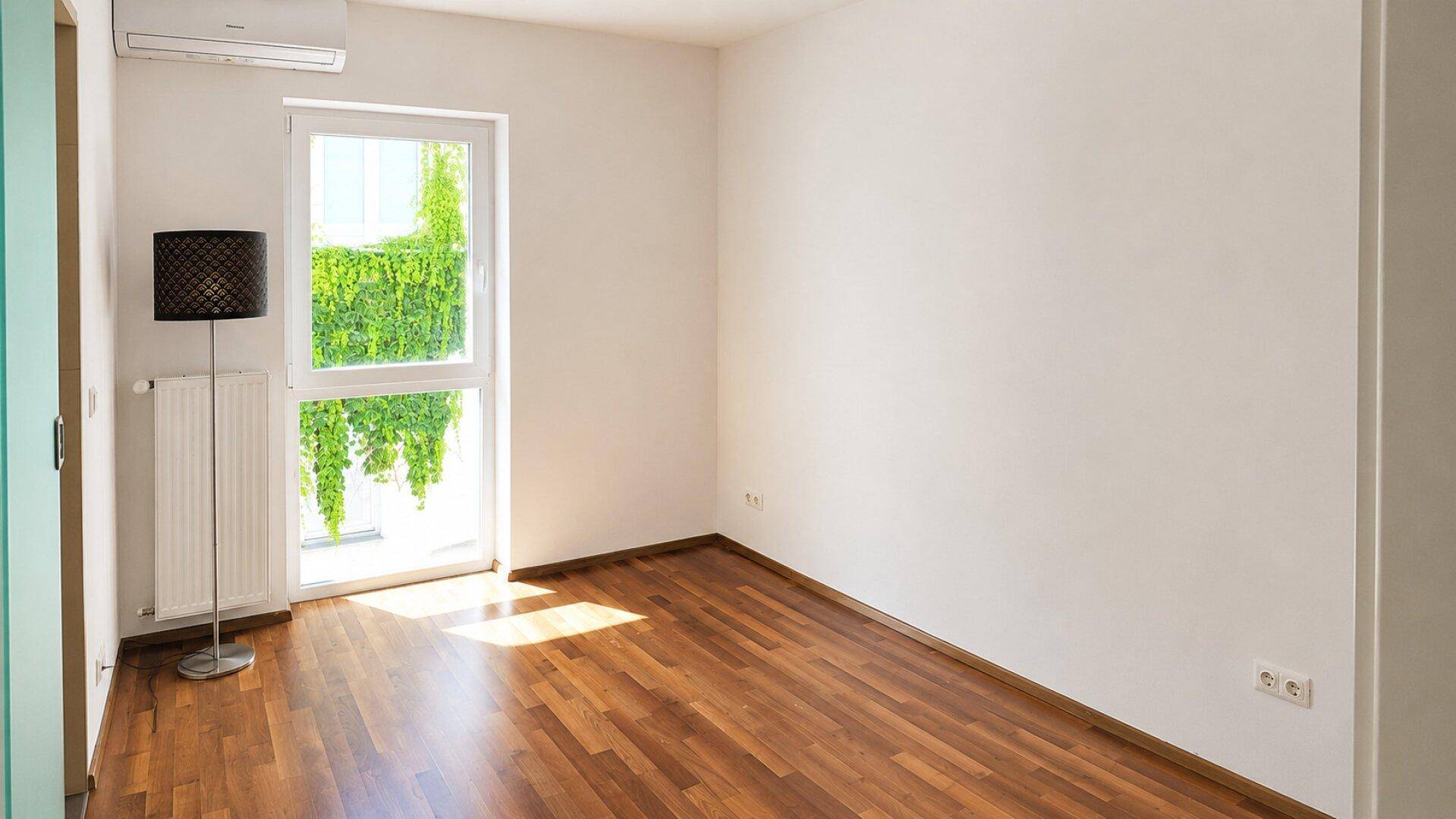 Heller Raum mit Holzboden, großem Fenster und Klimaanlage, ideal für Schlaf- oder Arbeitszimmer.