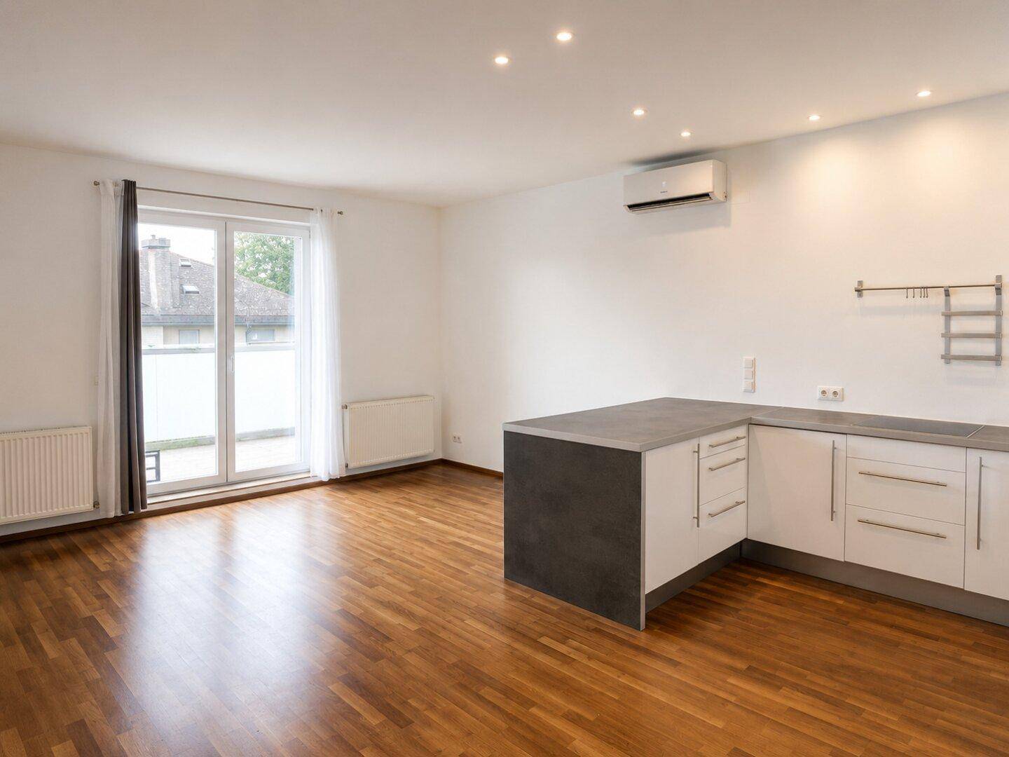 Offener Wohnbereich mit Holzboden, Klimaanlage und Zugang zu einem Balkon oder einer Terrasse.