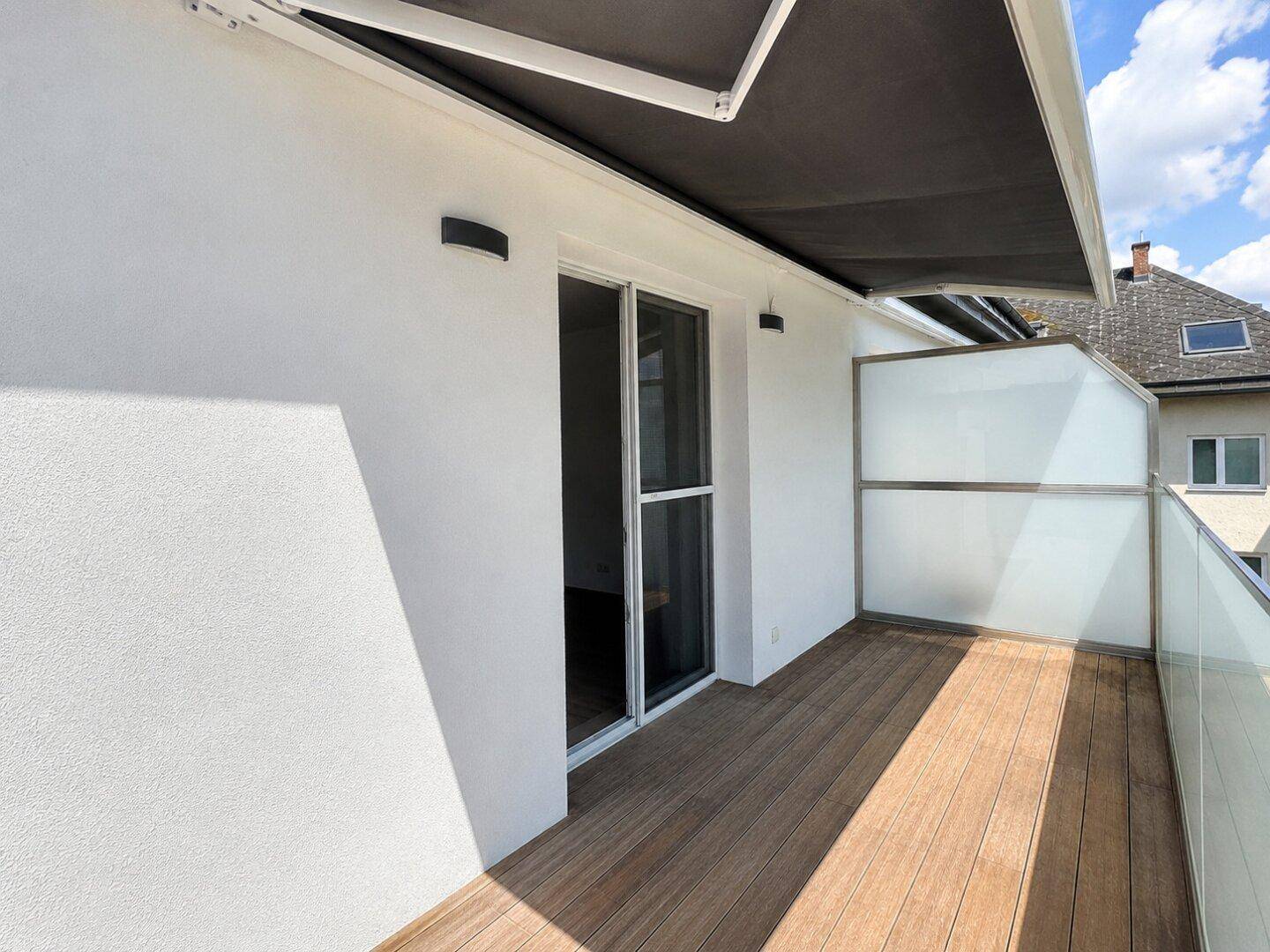 Geräumiger Balkon mit Holzboden, Glasbrüstung und ausfahrbarer Markise für angenehmen Schatten.