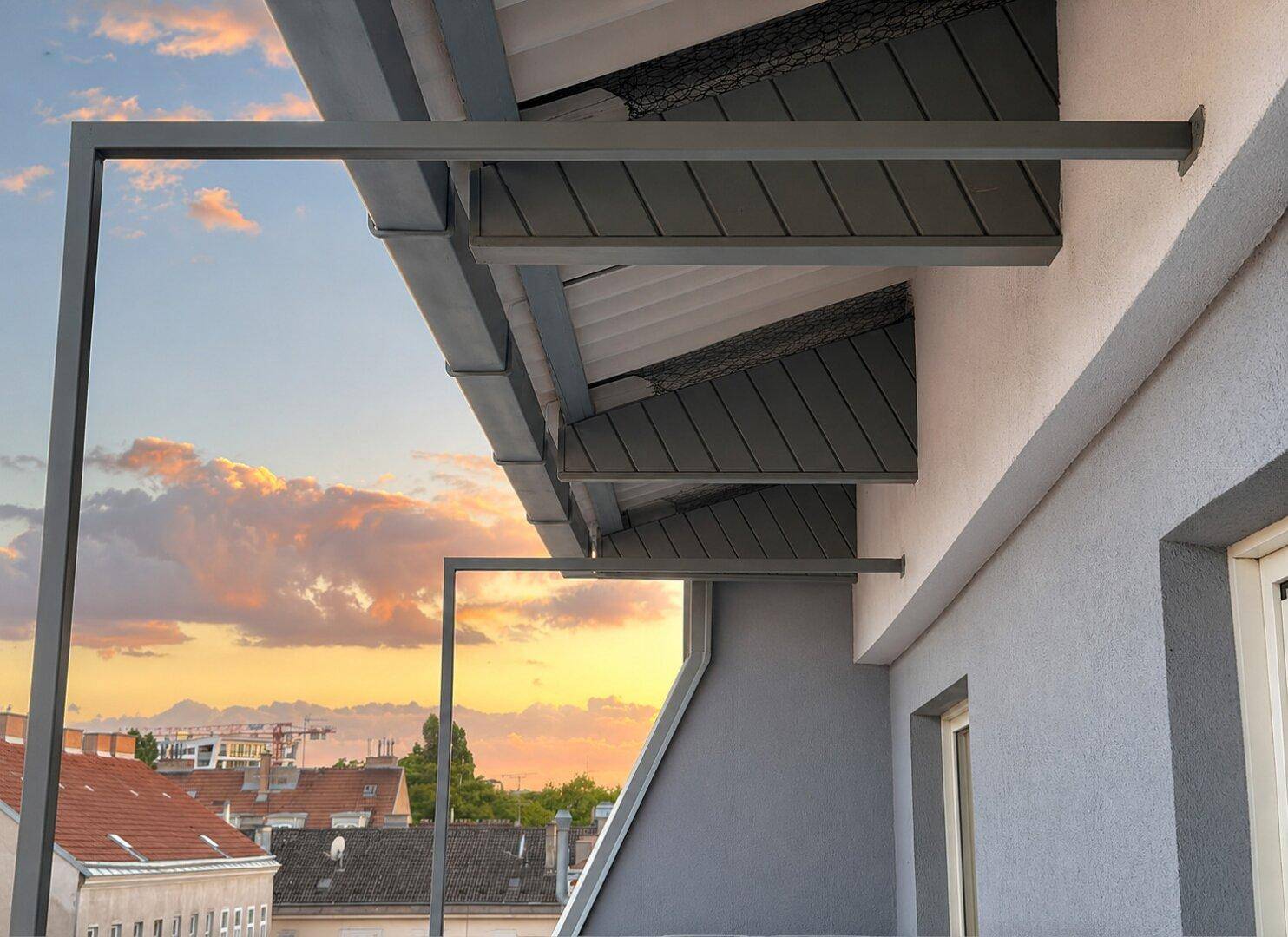 Architektonische Details der Gebäudefassade mit Balkonstruktur vor einem farbenprächtigen Sonnenuntergang.