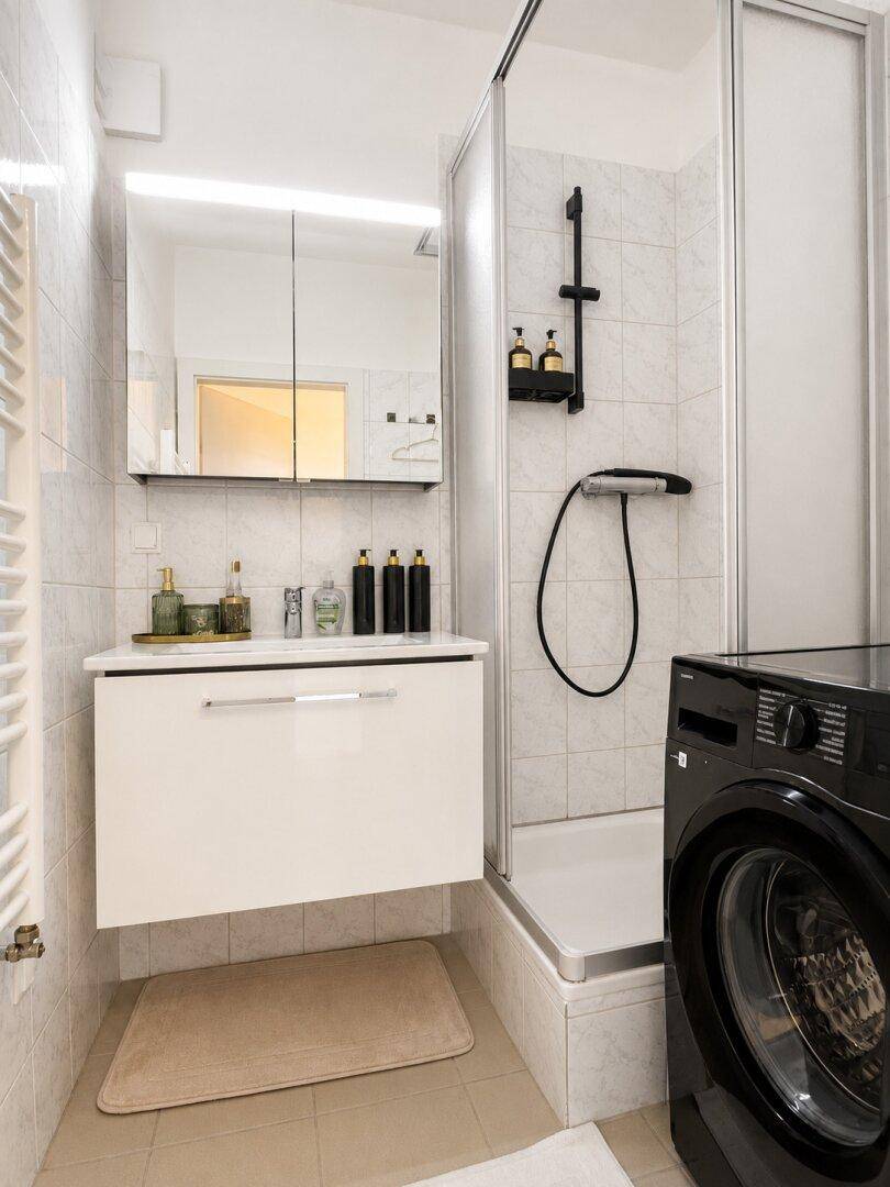 Modernes Badezimmer mit Duschkabine, Waschbeckenunterschrank, Spiegelschrank und integrierter Waschmaschine.
