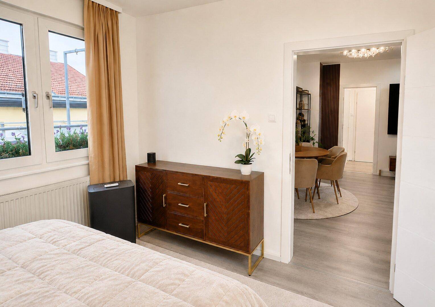 Gemütliches Schlafzimmer mit Holzkredenz und Blick in den offenen Wohnbereich, durchflutet von Tageslicht.