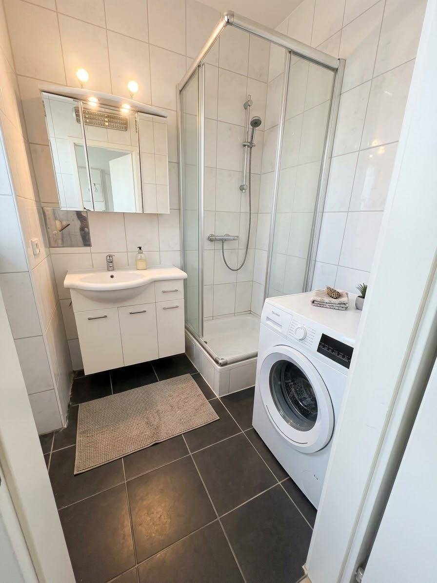 Modernes Badezimmer mit Dusche, Waschmaschine und weißen Fliesen.