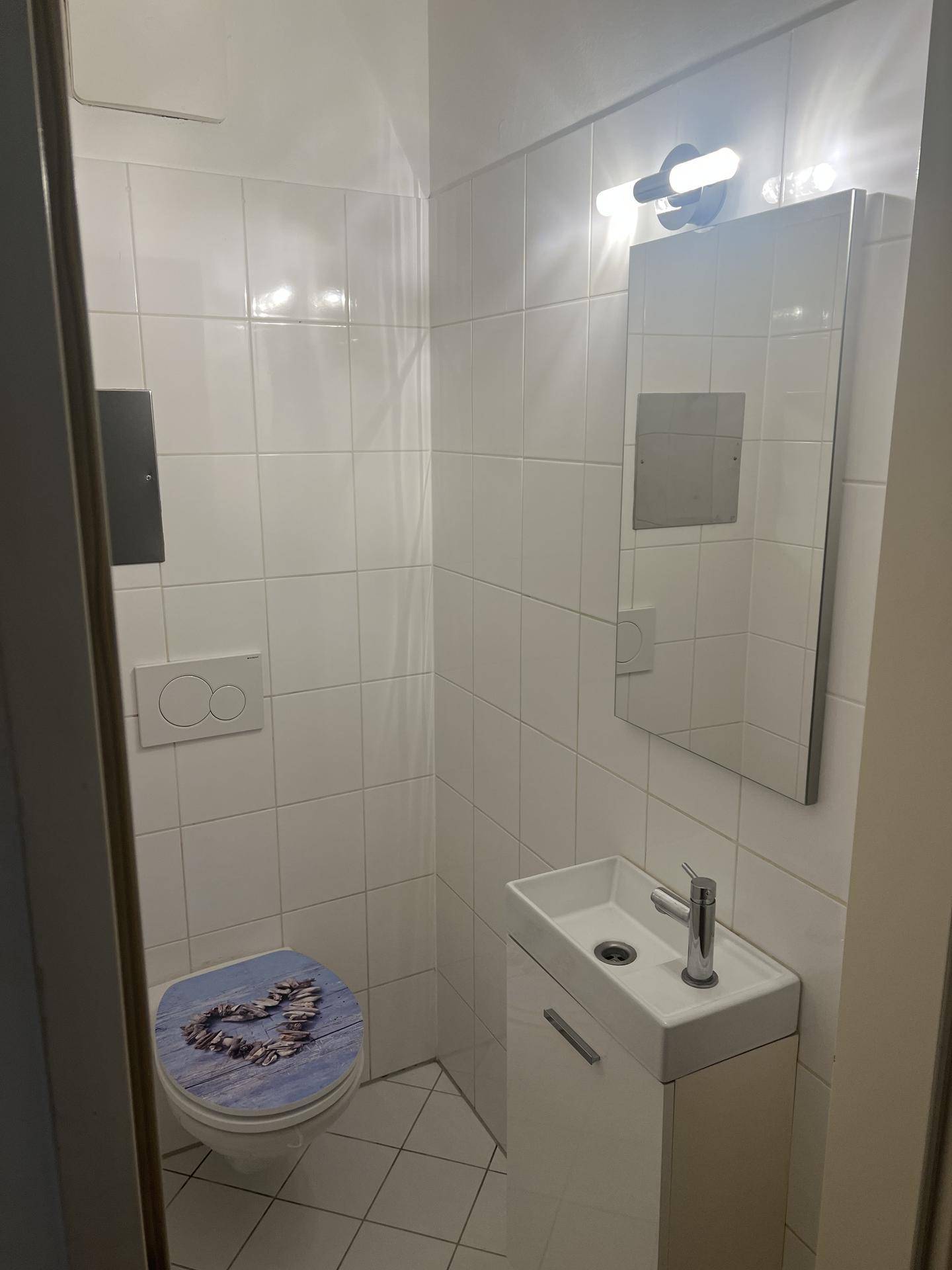 Modernes Gäste-WC mit weiß gefliesten Wänden, wandhängender Toilette und kleinem Waschbecken.