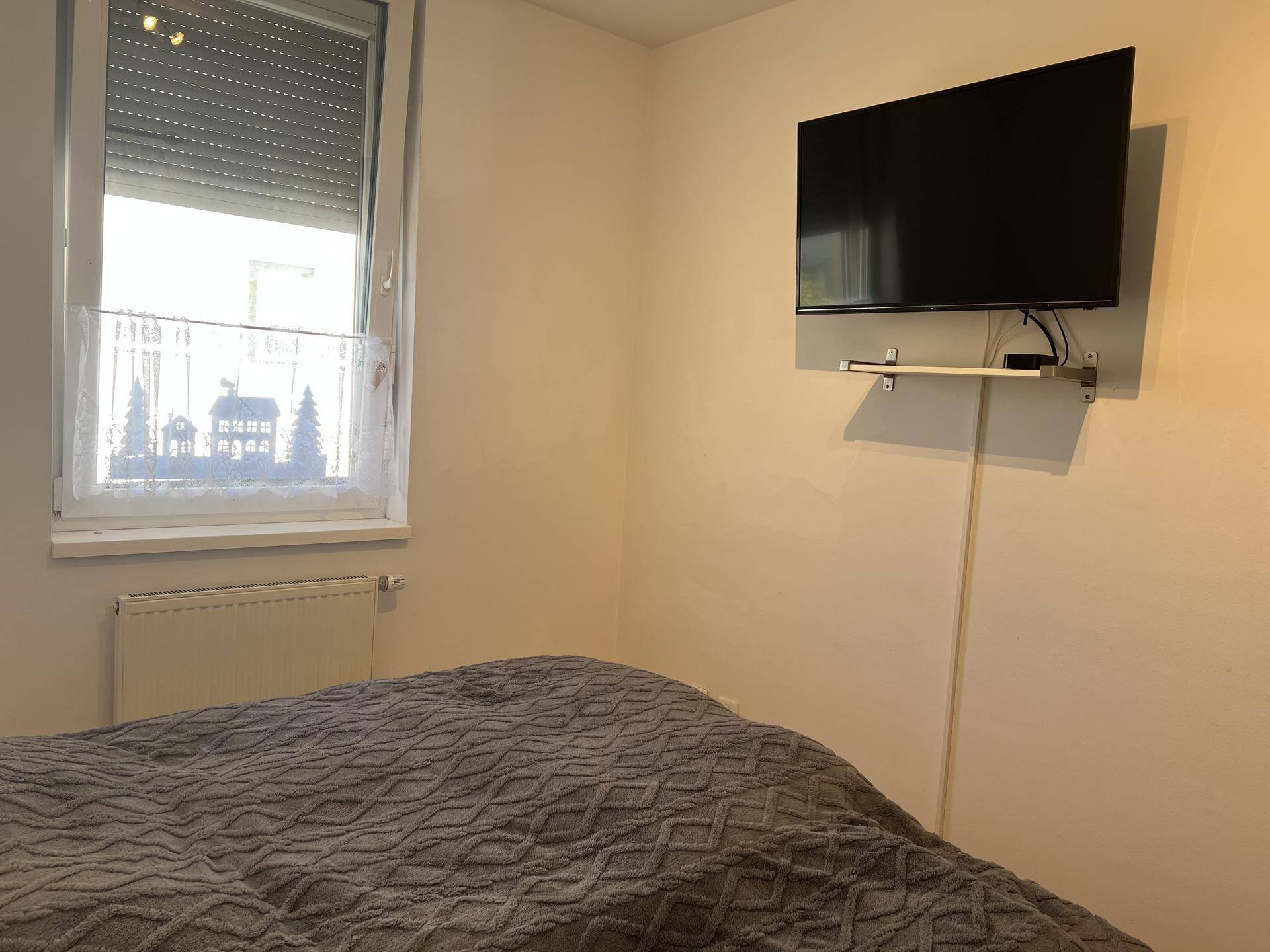 Schlafzimmer mit einem an der Wand montierten Fernseher und einem Fenster mit Rollladen.
