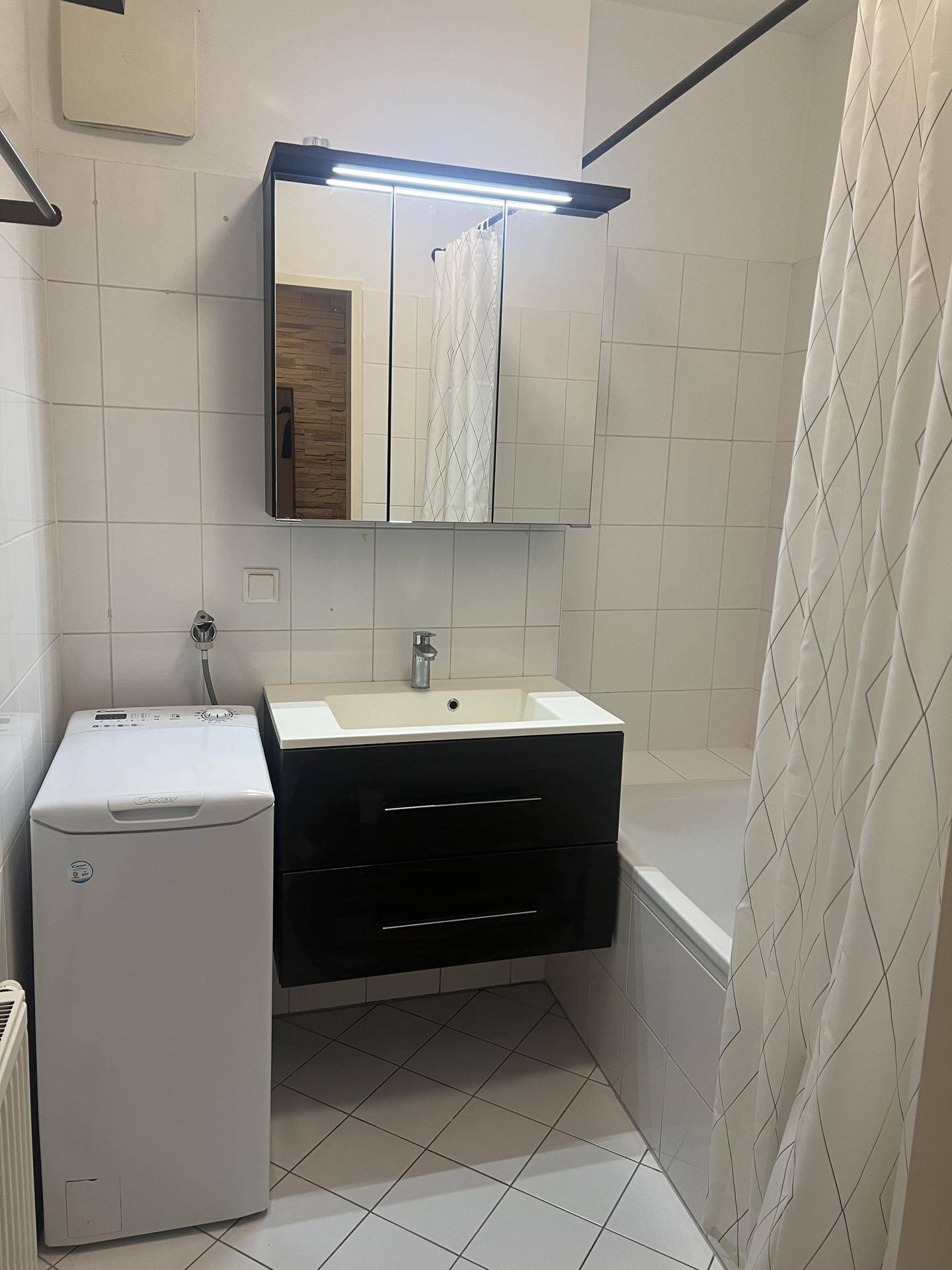 Badezimmer mit Badewanne, Waschbeckenunterschrank, Spiegelschrank und Waschmaschine.