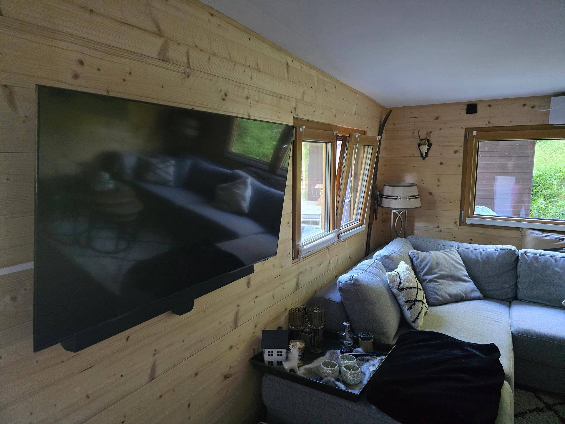 Wohnzimmer mit Holzwänden, großem Fernseher und bequemer Eckcouch.
