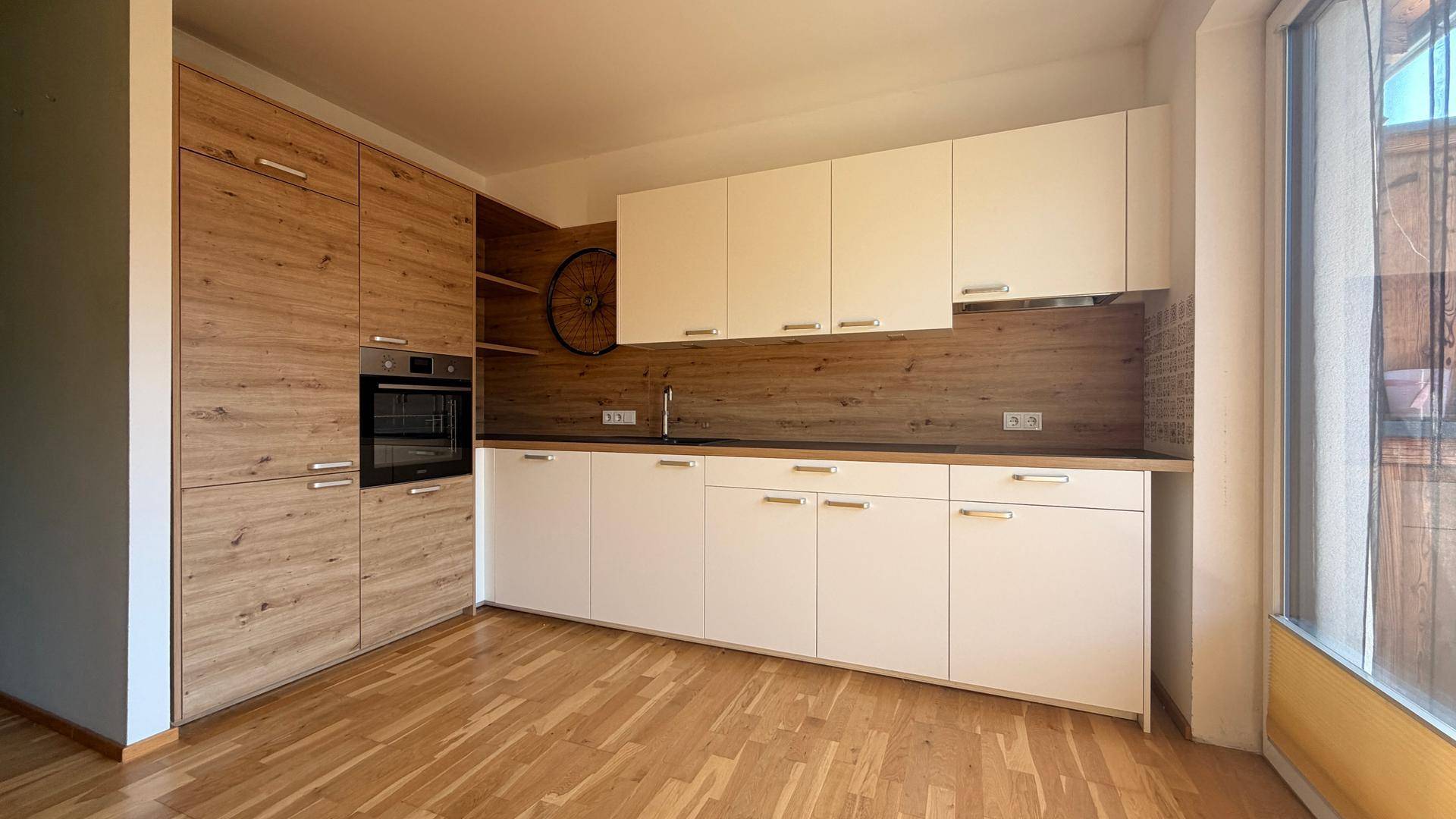 Moderne Einbauküche mit hellen Holzfronten, weißen Oberschränken und integriertem Backofen.