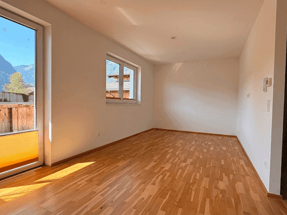 Helles Zimmer mit Holzboden, weißen Wänden und Zugang zu einem Außenbereich mit Bergblick.