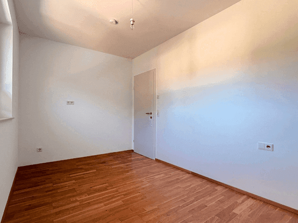Geräumiges Zimmer mit Holzboden und weißen Wänden, bereit für individuelle Gestaltung.