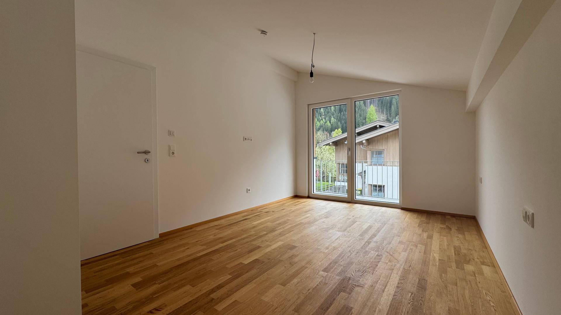 Helles Zimmer mit Holzboden, Dachschräge und großem Fenster mit Blick ins Grüne.