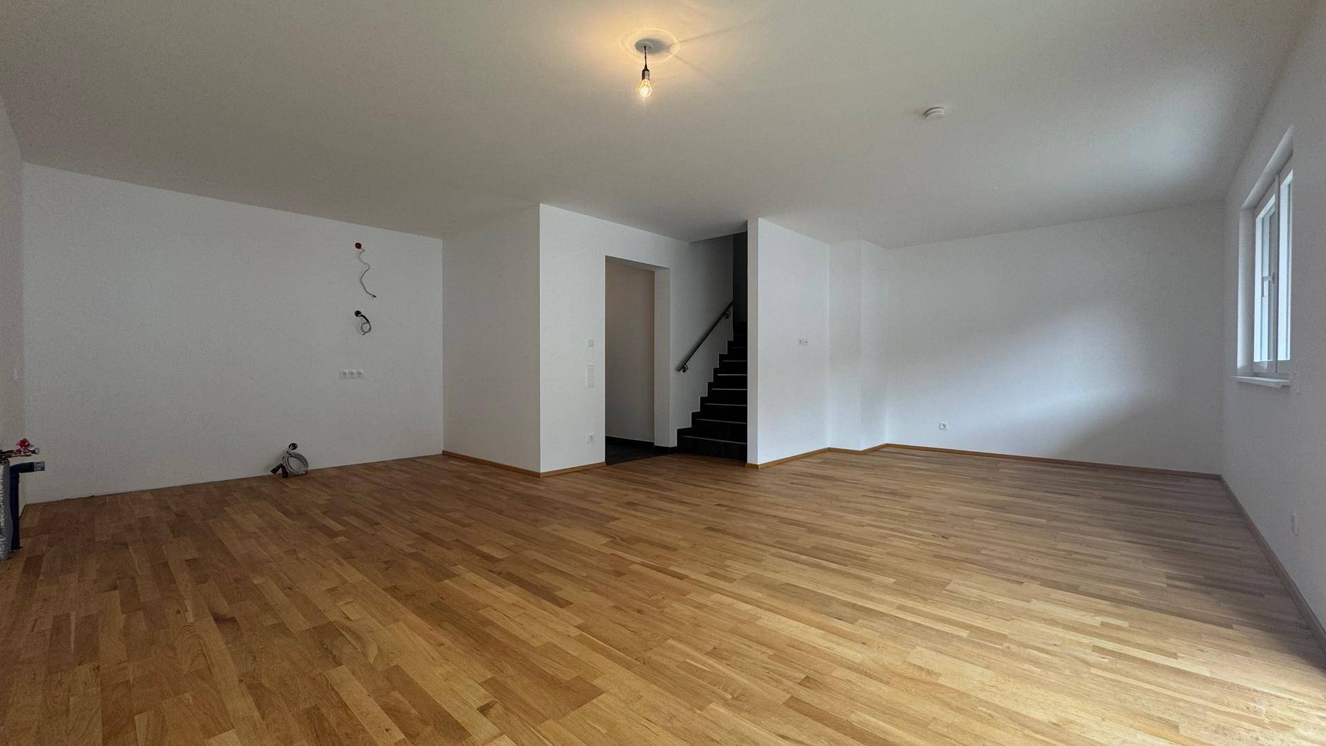 Geräumiger, unmöblierter Raum mit Holzboden und Treppenzugang, bietet vielseitige Nutzungsmöglichkeiten.
