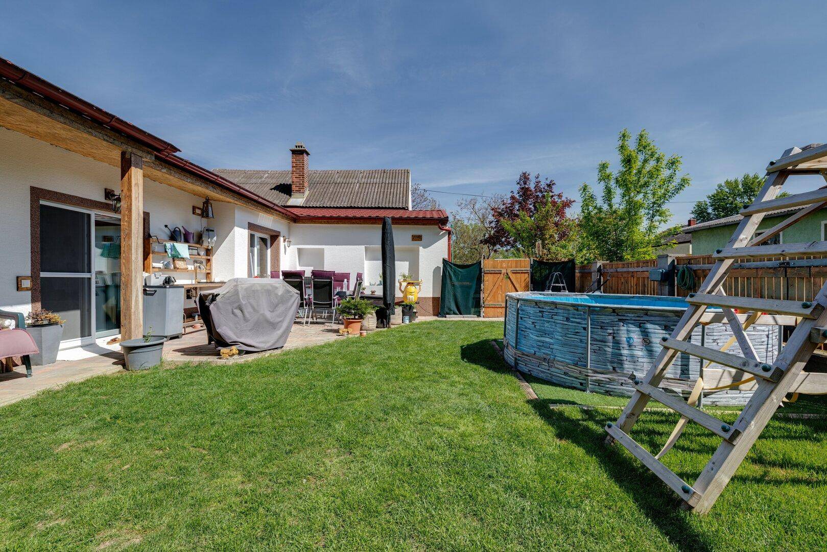 Weitläufiger Garten mit Rasen, Pool, Spielgeräten und einer überdachten Terrasse am Haus.