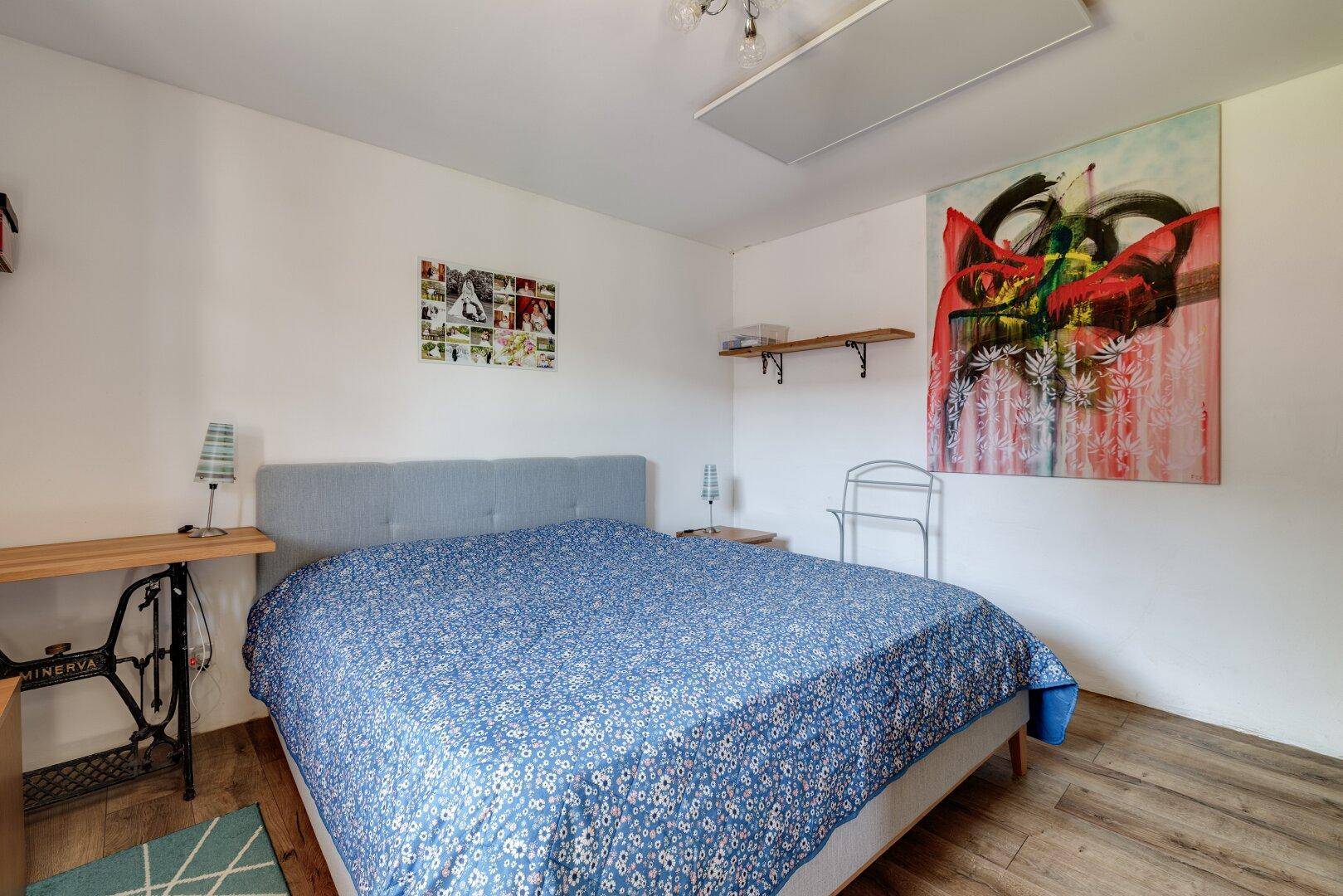 Gemütliches Schlafzimmer mit Doppelbett, Holzoptikboden und einem modernen Kunstwerk an der Wand.
